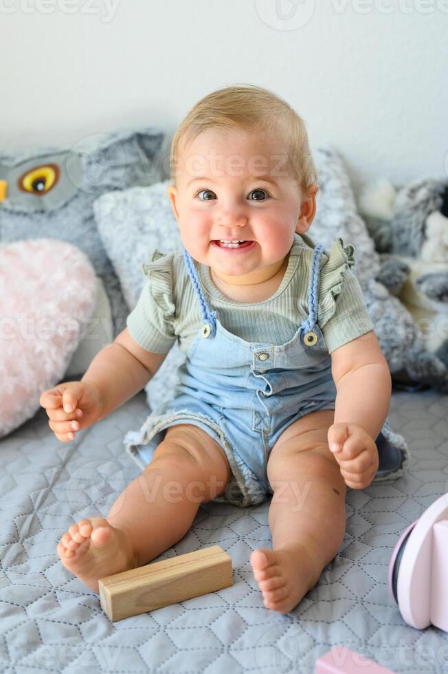 Cheerful toddler sitting on bed near toy block at home photo