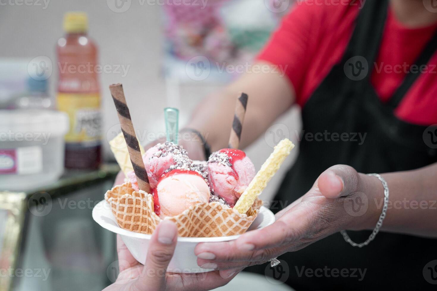 An adult Hispanic woman is serving a traditional Mexican ice cream with toppings to a client photo