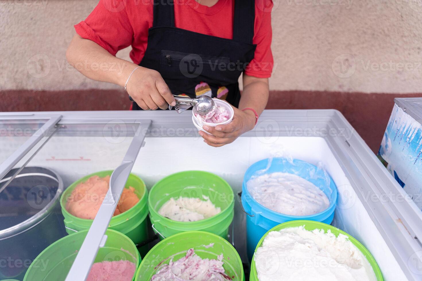 An Hispanic adult woman is serving blackberry and cheese ice cream on a cup in the street photo