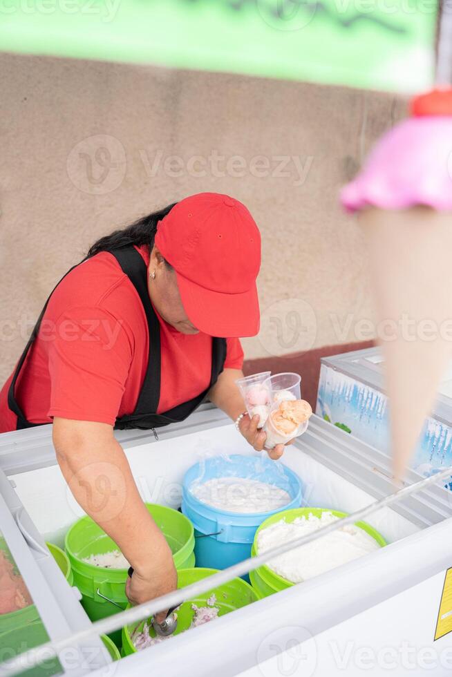 An Hispanic adult woman is serving some ice cream in plastic cups in the street photo