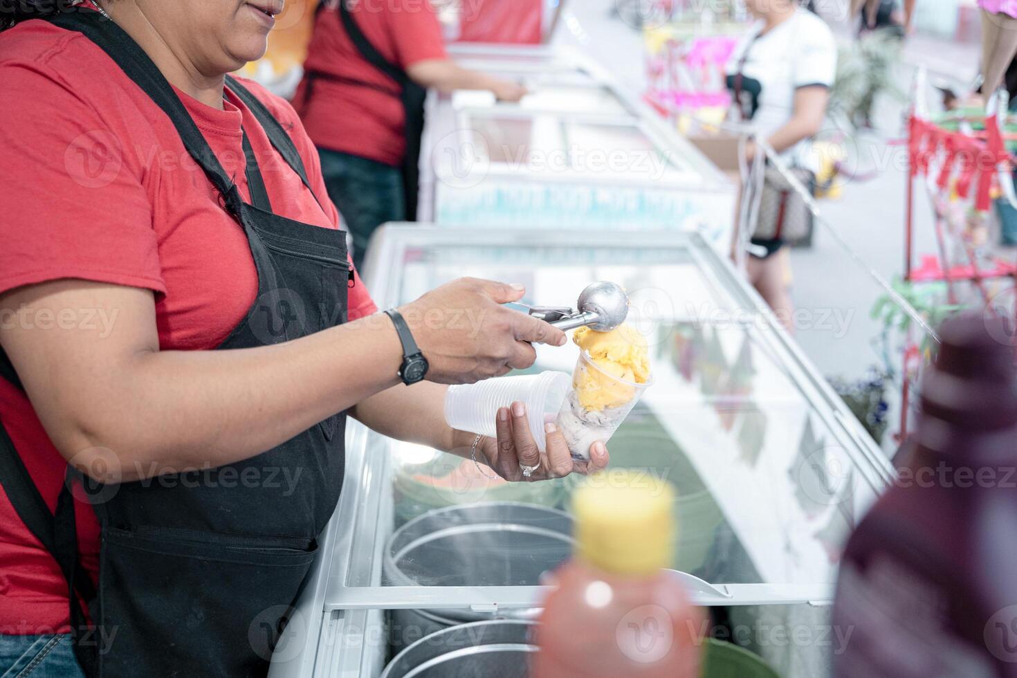 An Hispanic adult woman is serving some vanilla ice cream balls in a cup in the street photo