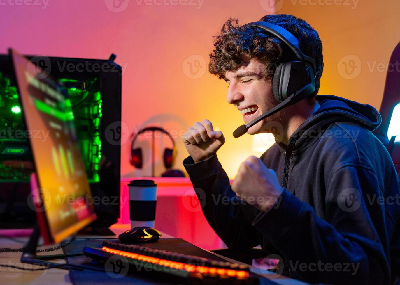 Young teenager plays the computer and celebrates victory in game with a clenched fist and a smile. photo