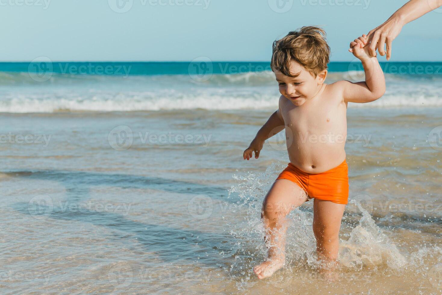 Happy cute boy walking in sea water near parent photo
