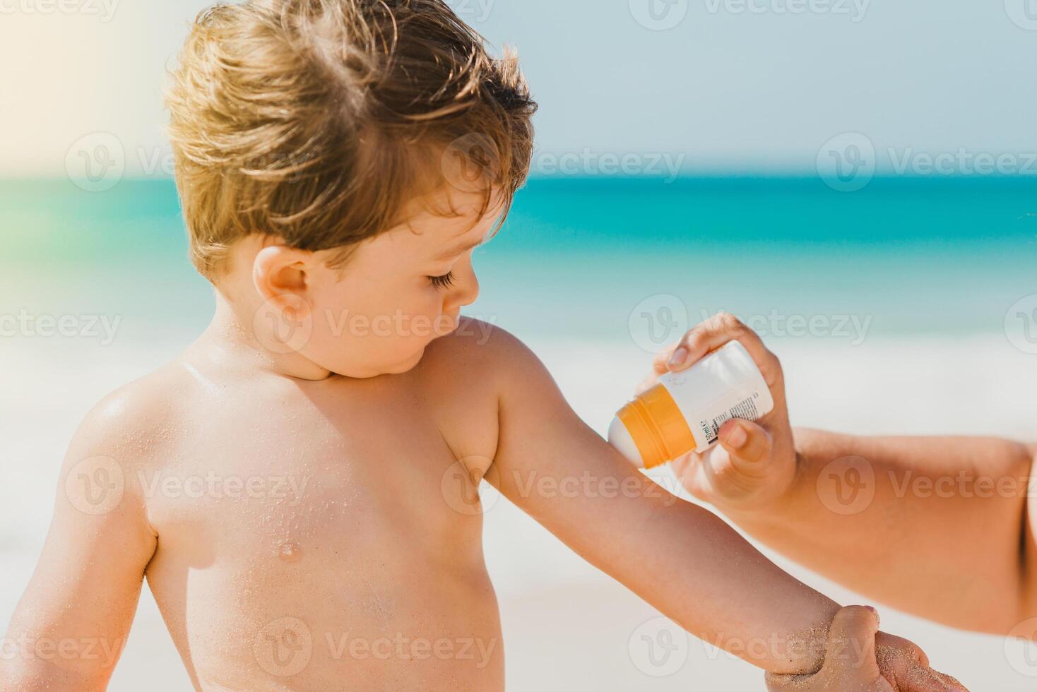 Mother with sunscreen cream taking care of baby on beach photo