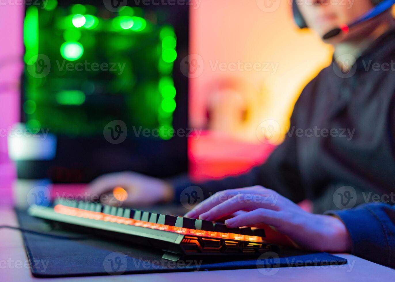 Unrecognizable young gamer with hands on illuminated keyboard in room with colored background photo