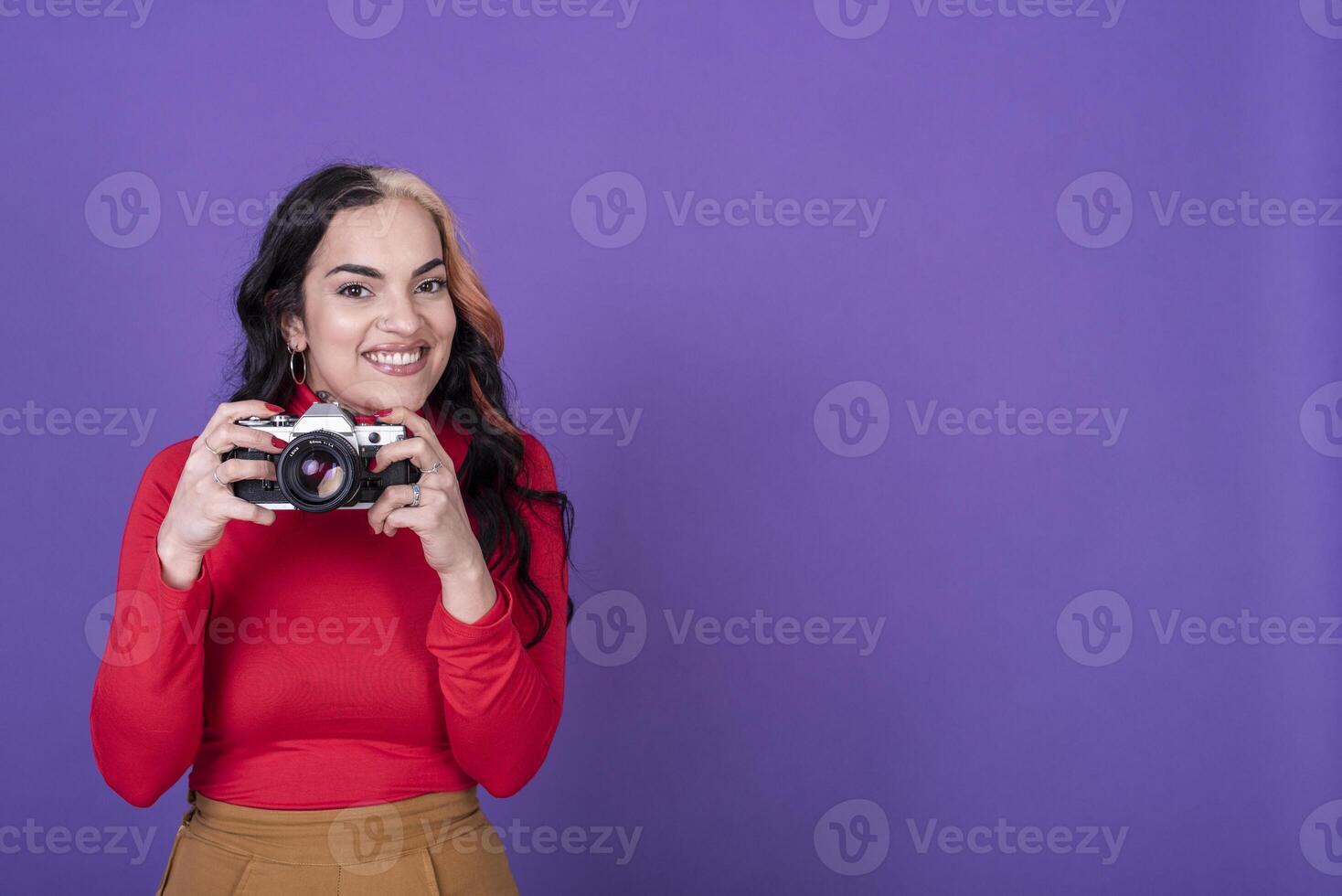 Attractive young lady taking a photo with her film camera over a violet background. Copy space.