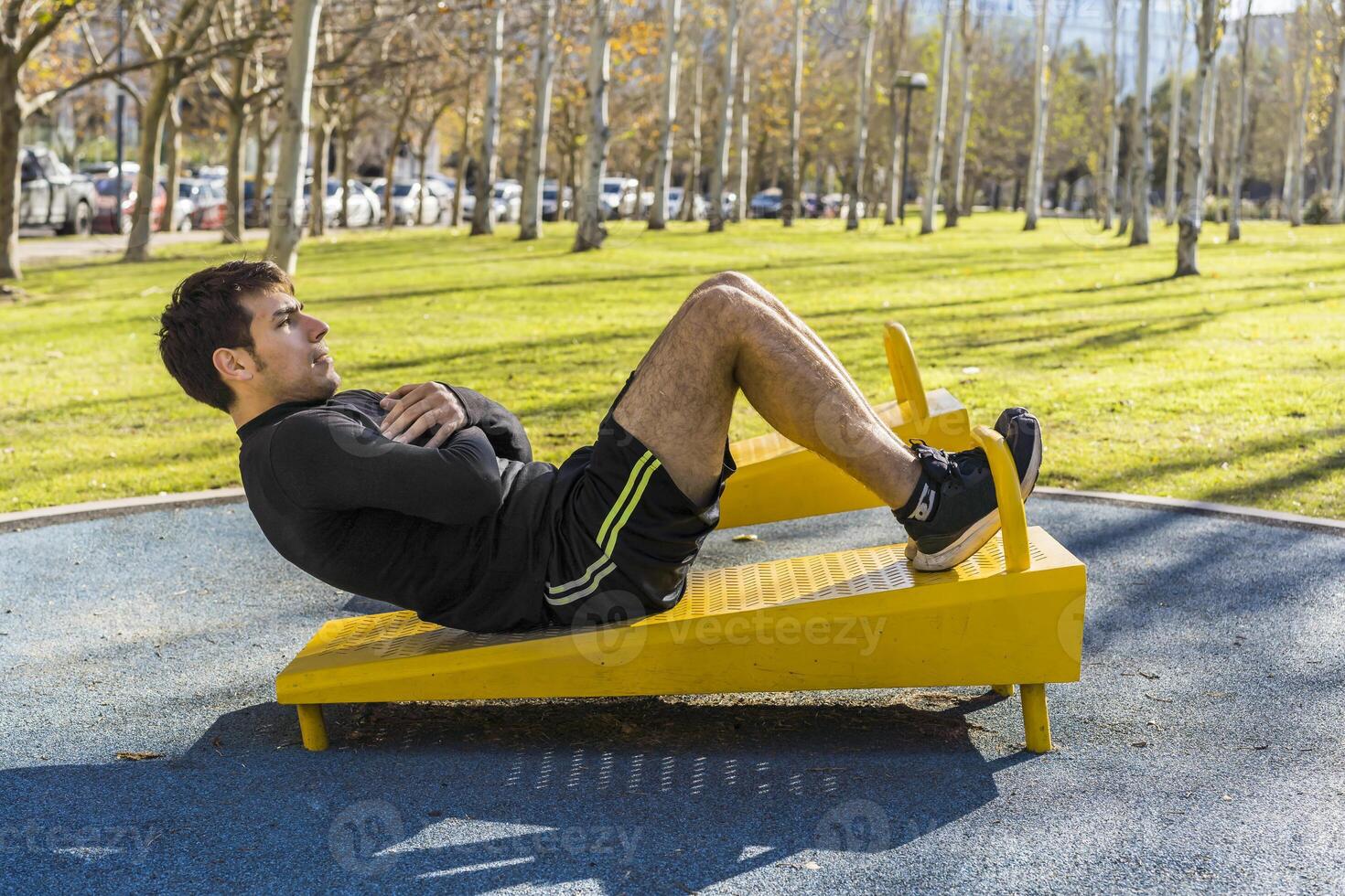 Attractive young man doing abdominal exercises on a public equipment in outdoor fitness photo