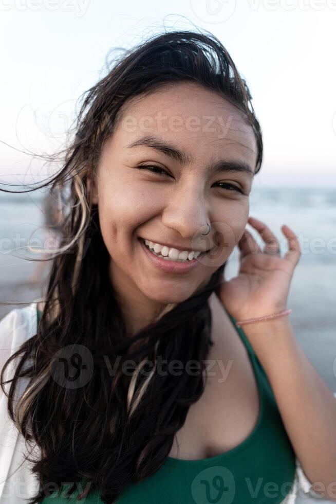 Portrait of a young Hispanic woman smiling in front of the sea at the beach photo