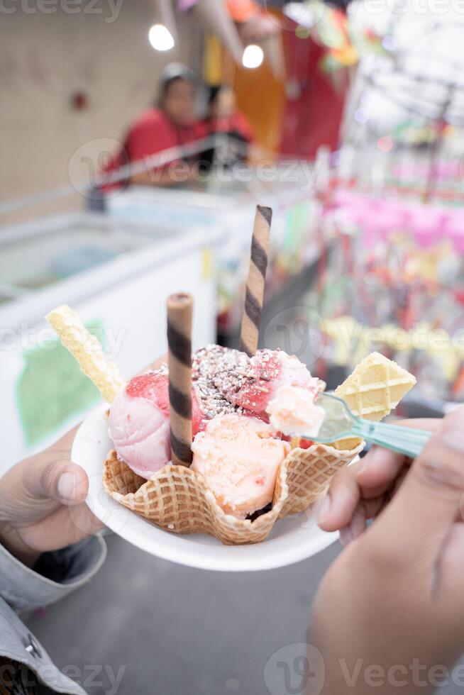 A young Hispanic woman is eating a traditional ice cream in front of a street market stall photo