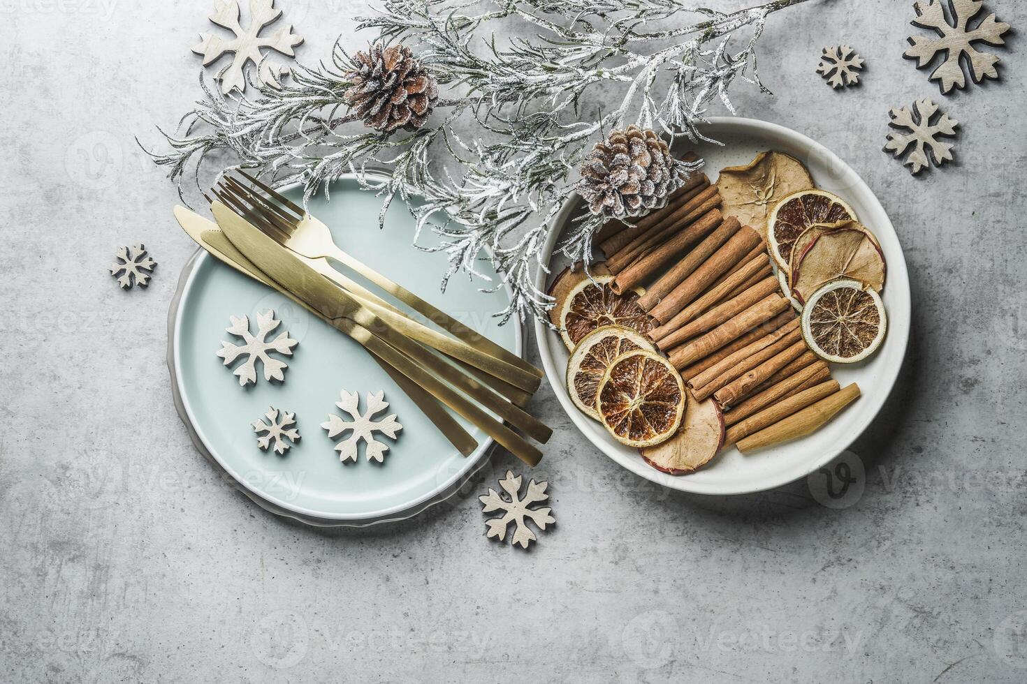 Christmas table setting with golden cutlery, pale blue plate, cinnamon sticks, dried orange natural dried apples and oranges and winter branches on grey table. Top view. photo