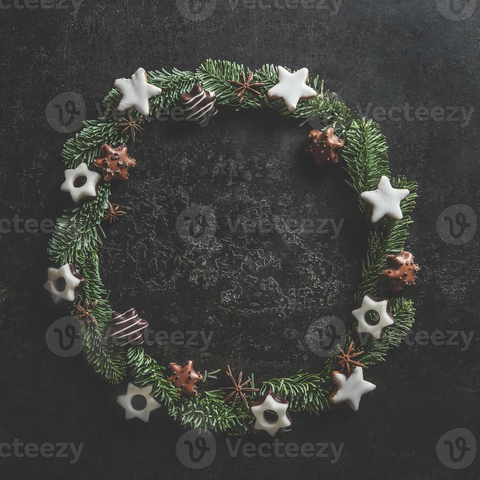 Christmas circle frame made with fir wreath and cookies on dark concrete kitchen table. Christmas background with copy space. Top view. photo