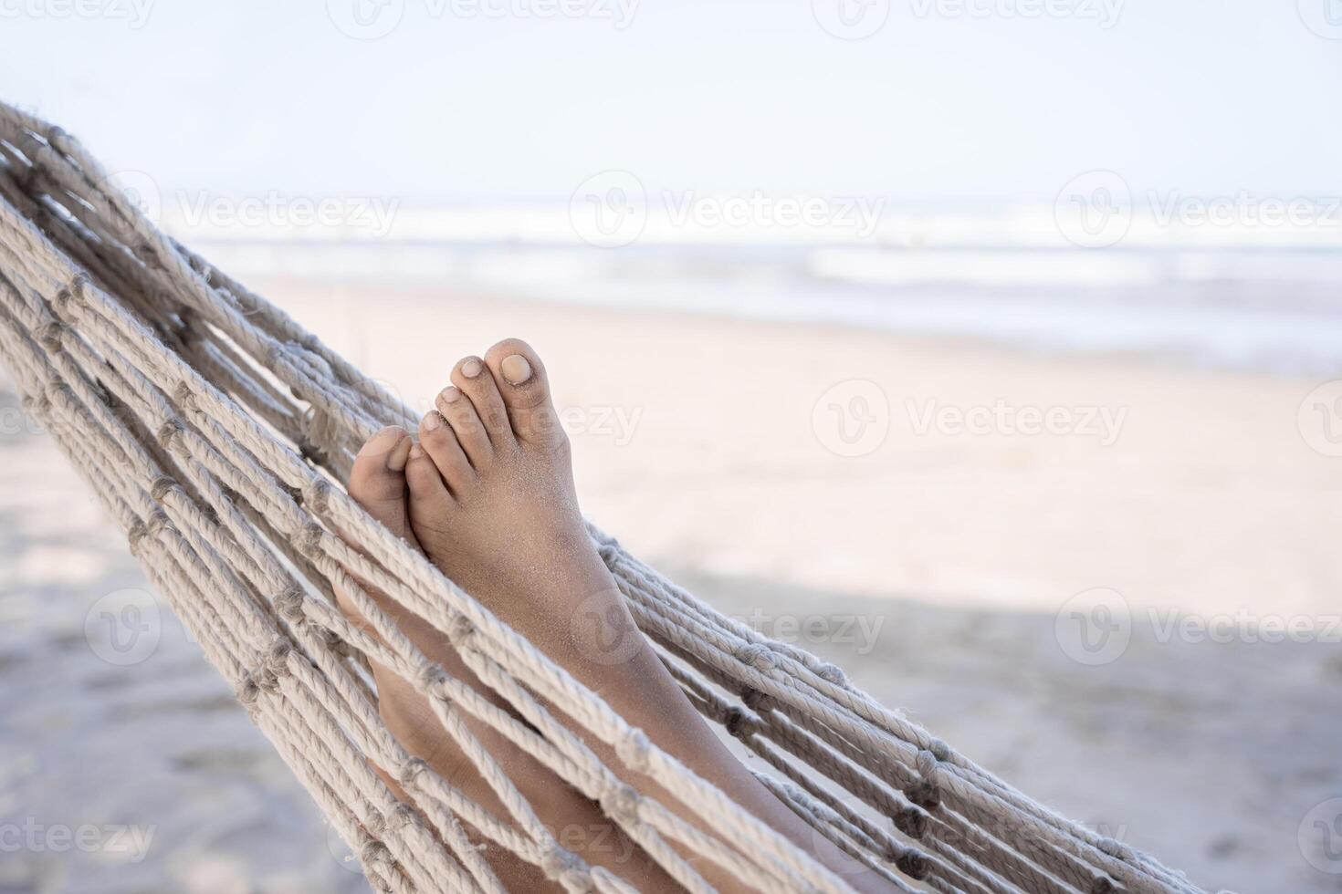 A close-up of a young Hispanic woman's sandy feet as she lounges on a hammock at the beach. photo