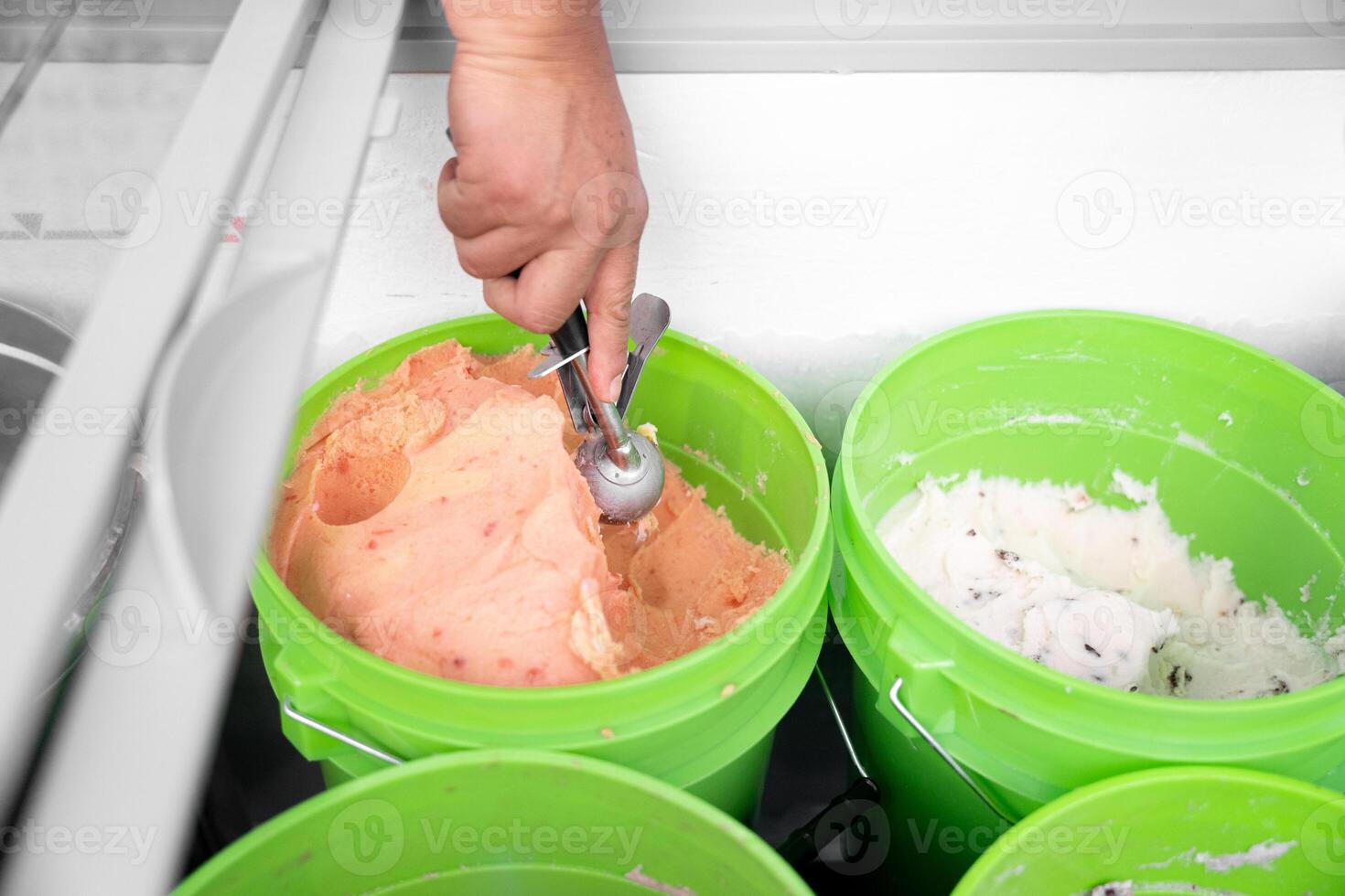 An Hispanic adult woman is taking mamey ice cream with a spoon from a bucket. Close up photo