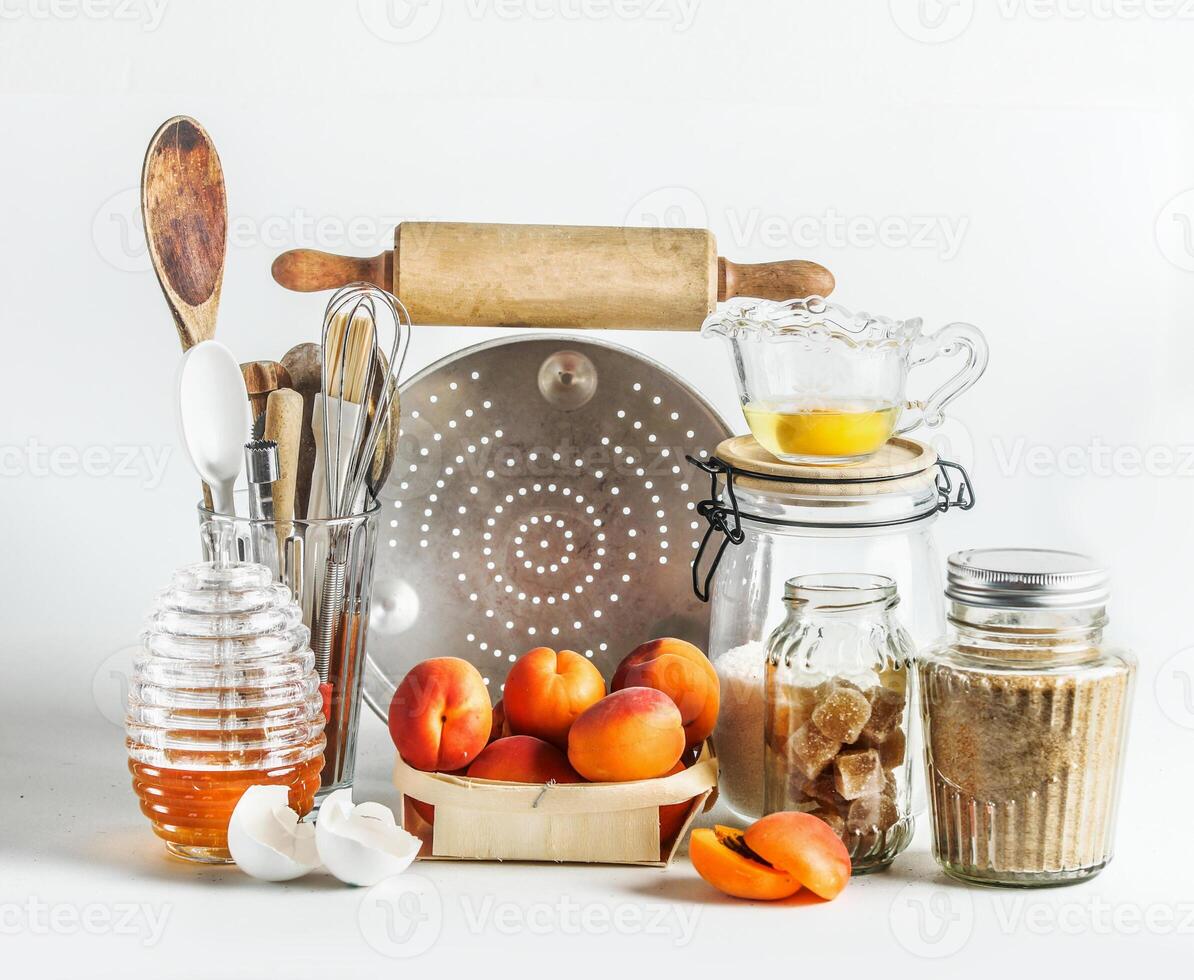 Baking setting with apricots, kitchen utensils, tools, honey and ingredients at white background. Baking with seasonal fruit at home. Front view. photo