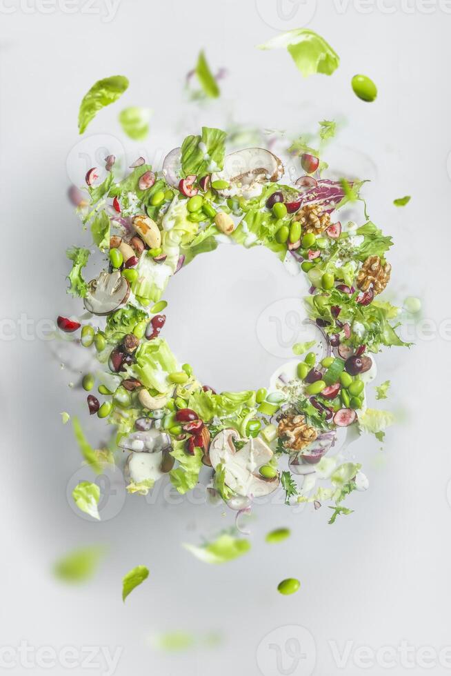 Circle frame of flying healthy green salad with lettuce, nuts, beans, dressing and vegetables. Balanced vegan food with copy space. Levitation of food photo
