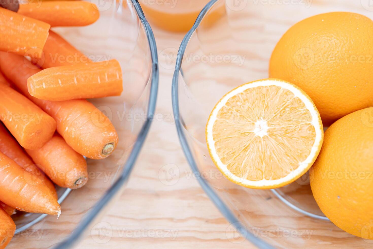 Some clean carrots and half oranges are ready to make juice inside of two dishes on a table photo