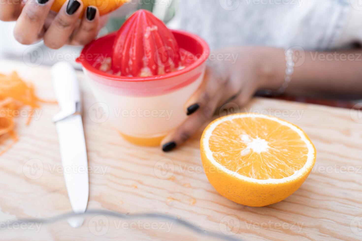 Close up of a young Hispanic woman is squeezing an orange to make orange and carrot juice outdoors photo