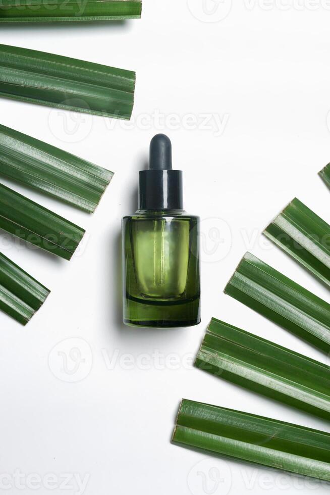 Green glass cosmetic bottle with pipete at white background with green palm leaves. Skin care with moisturizing face serum. Top view with copy space. photo