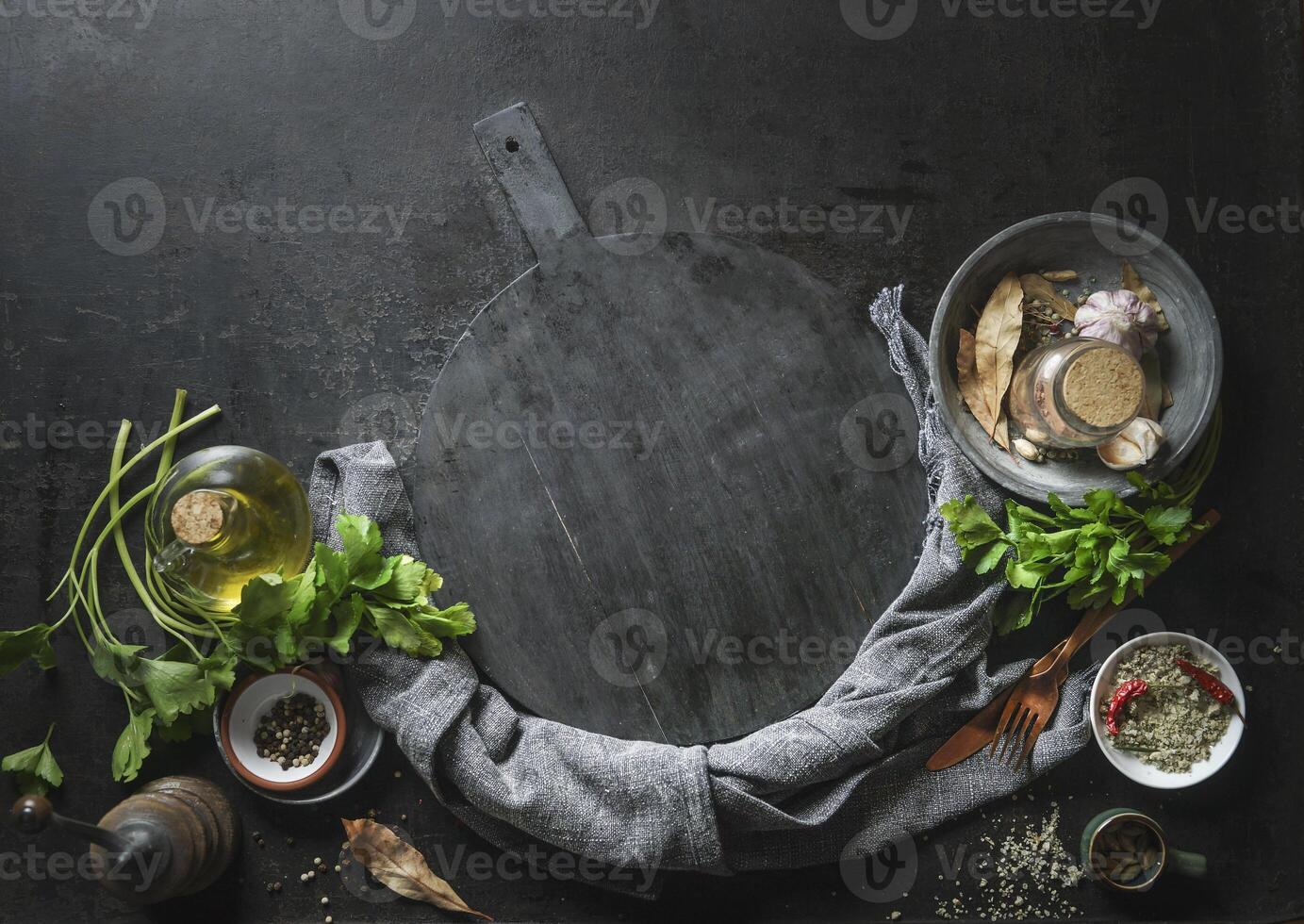 Kitchen flavor and seasoning ingredients with kitchen utensils around empty black cutting board. Top view. Frame photo