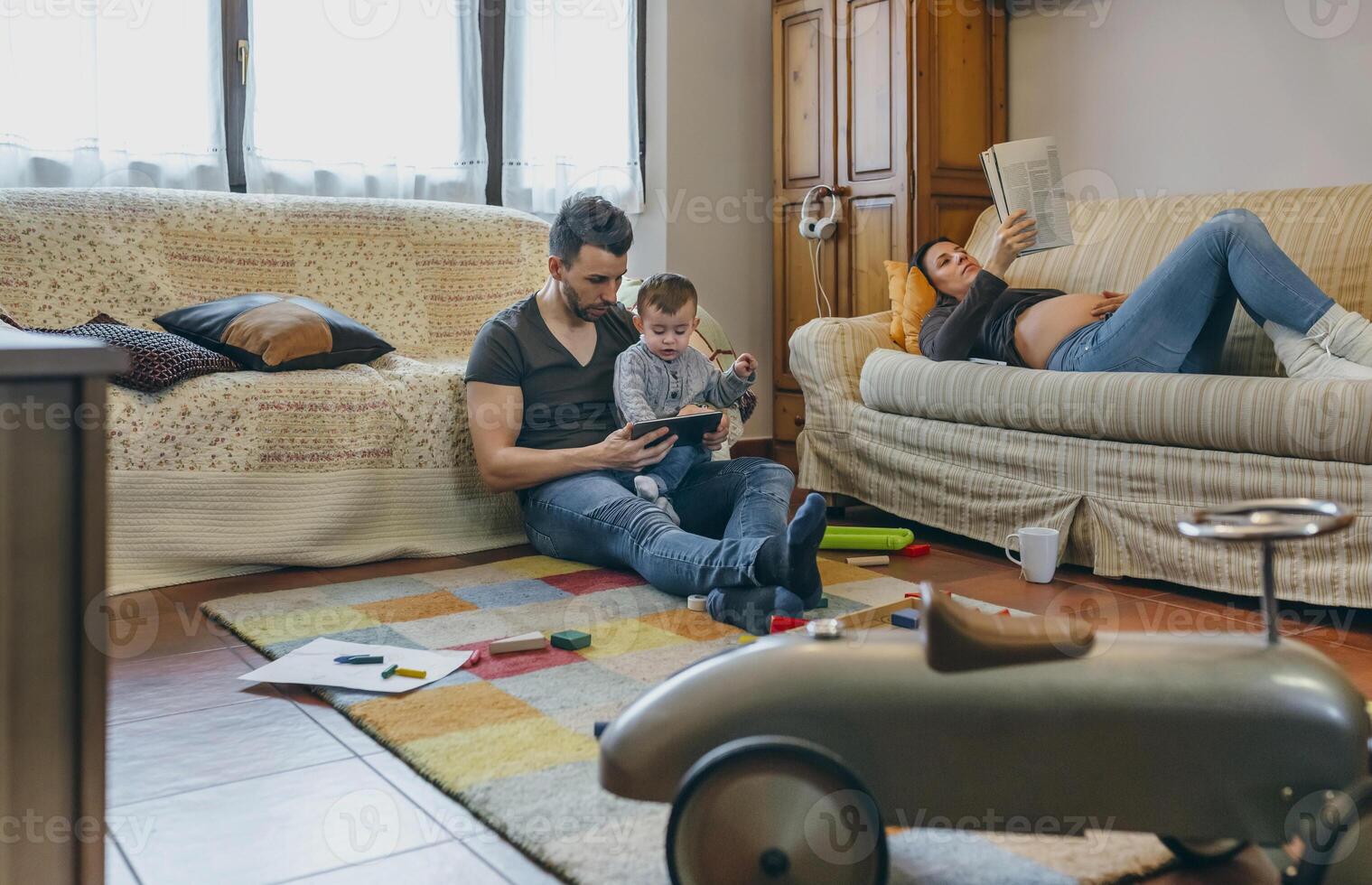 Father looking tablet with little son while the pregnant mother reads a magazine photo