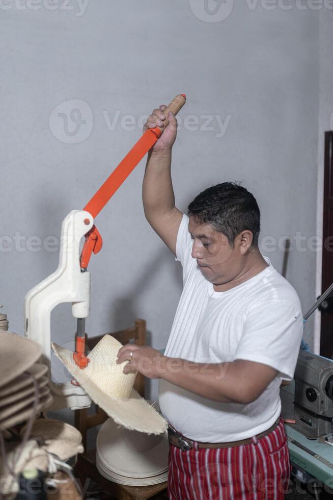An adult Hispanic man is making a hole in a natural fiber hat photo