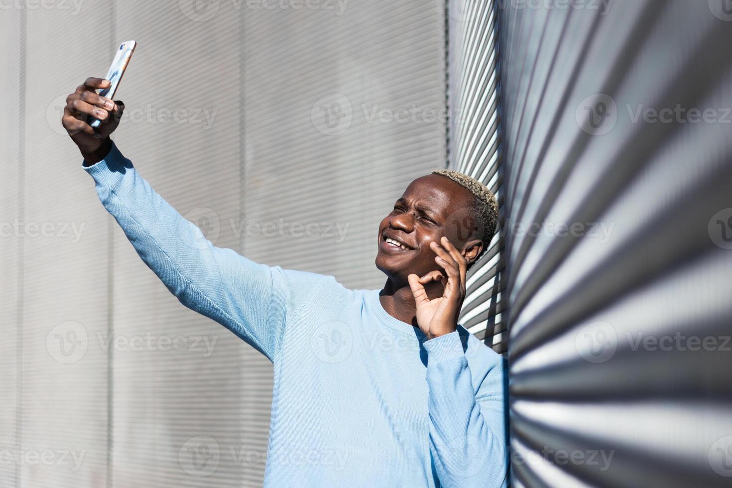 Cheerful young black guy doing OK sign while taking selfie on street photo