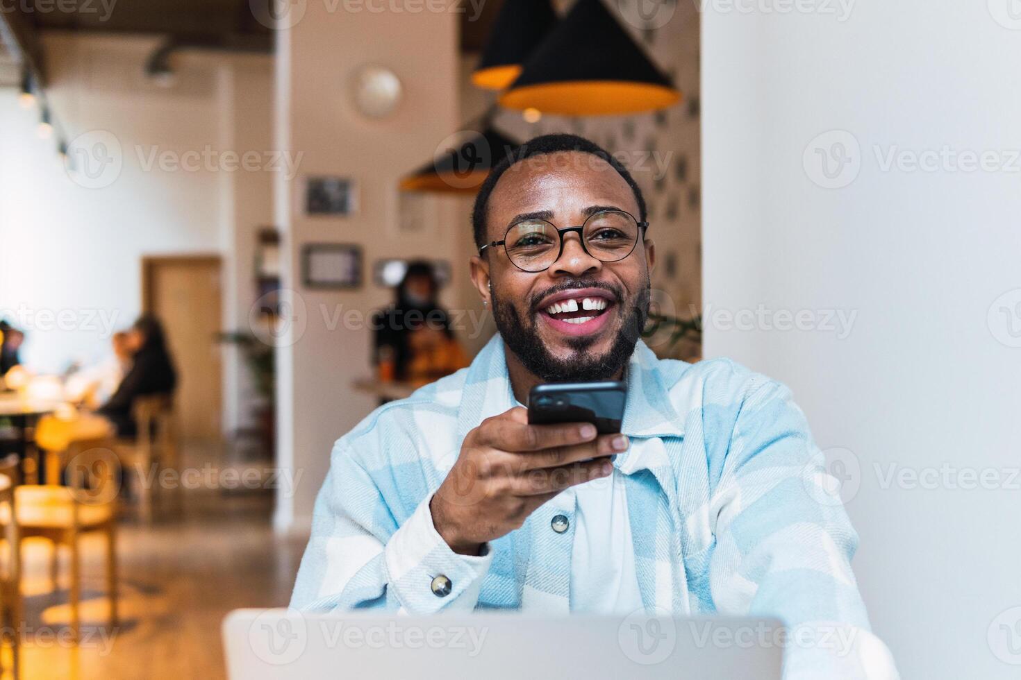 Smiling black man recording voice message in cafe photo
