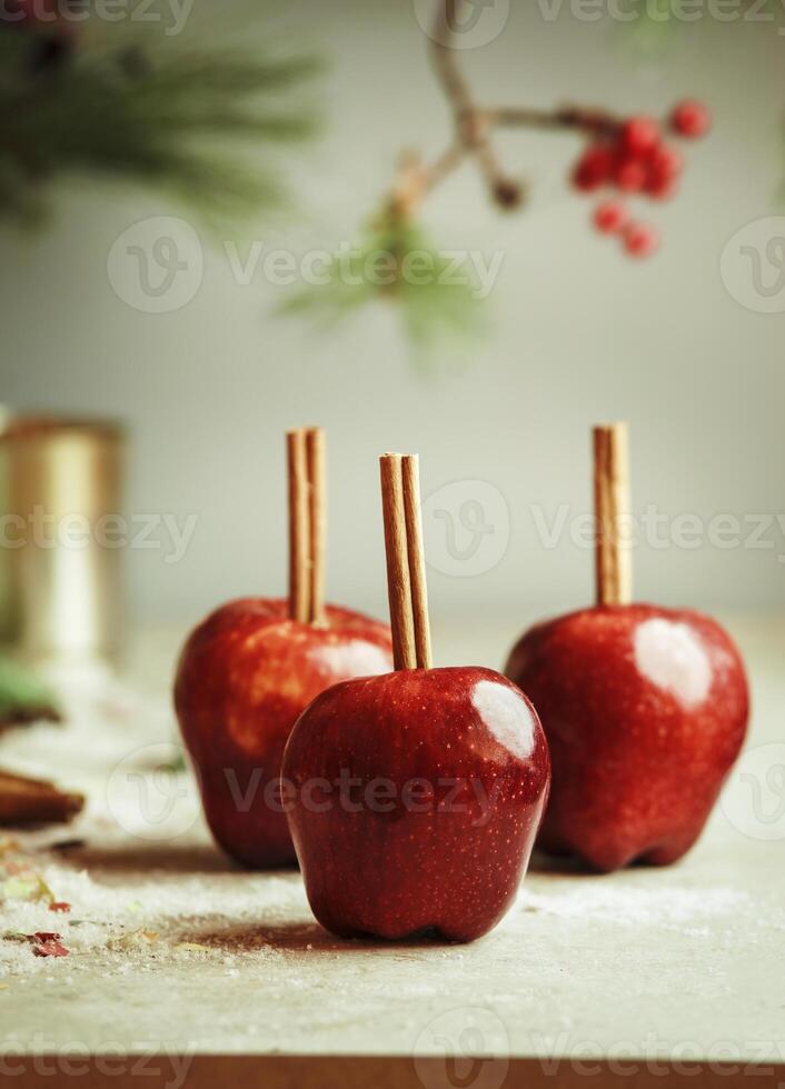 Red apples with cinnamon sticks on kitchen table with sugar at wall background with fir green. Sugar glazed apples. Delicious Christmas sweets. Front view. photo