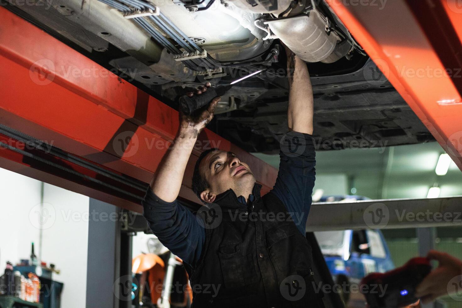 Adult repairman fixing car detail raised on lift in garage photo