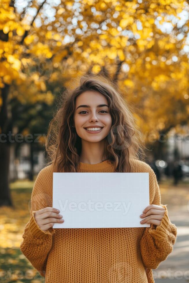 A smiling young woman holding a blank sign in the fall photo