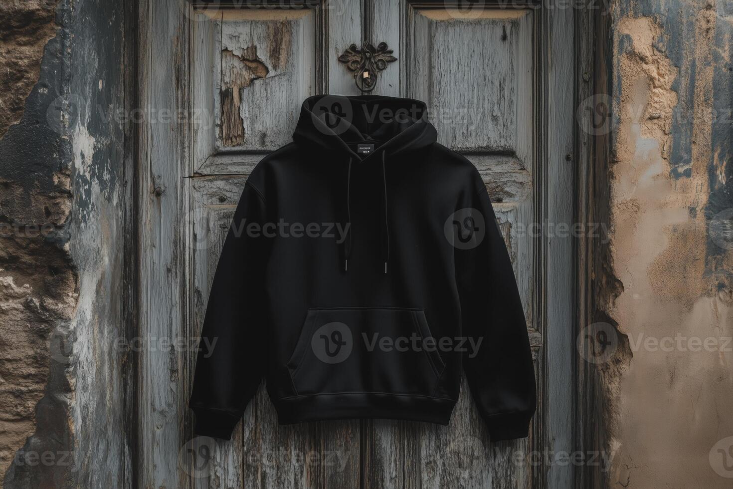 A black hoodie mockup hanging on an old, weathered wooden door with peeling paint. The door has a vintage design, adding a rustic charm to the scene. Sweatshirt with hood long sleeve for print. photo