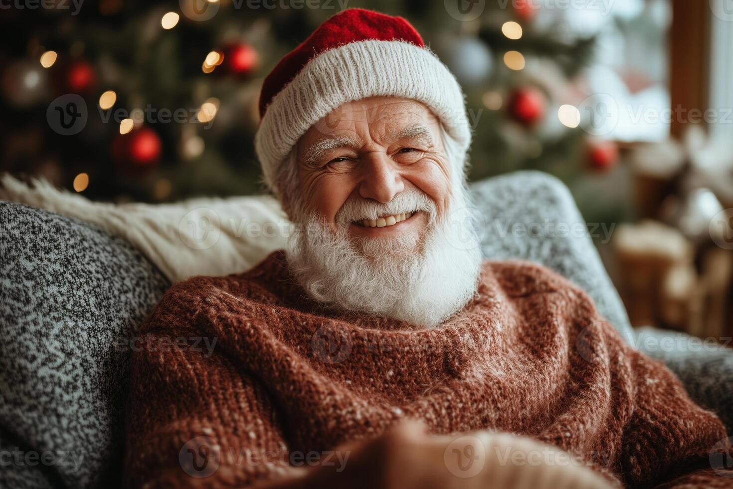 A smiling old man wearing a santa hat sitting on a couch photo