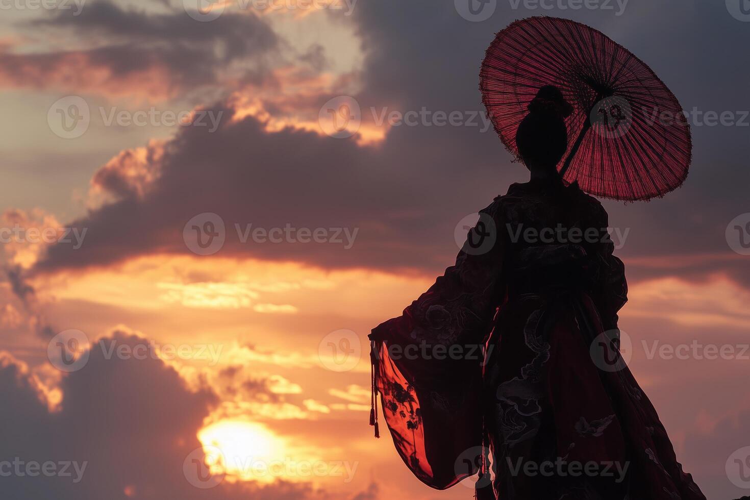 A silhouette of a person holding a red parasol against a vibrant sunset sky with clouds. The figure is dressed in traditional attire, creating a striking contrast with the colorful background. photo