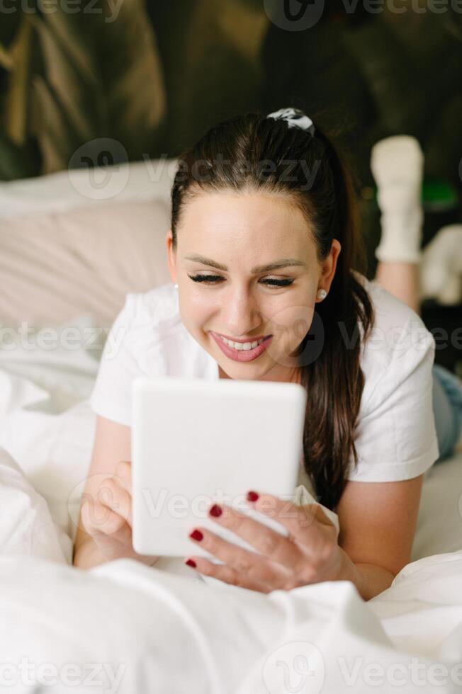 Smiling woman using tablet on bed in bedroom photo