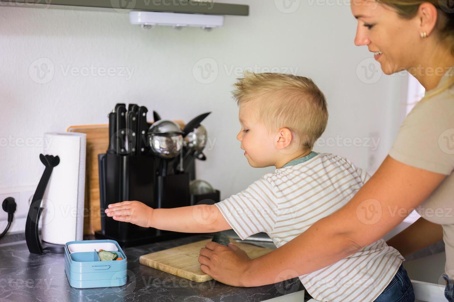 Happy crop mother and kid son with chopping board in kitchen in daylight photo