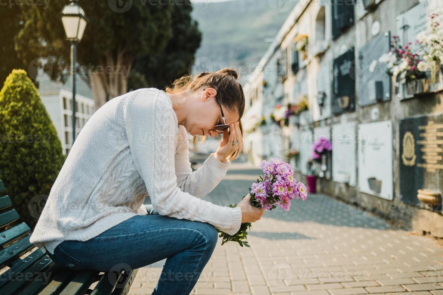 Sad woman crying sitting on bench with flowers in cemetery photo