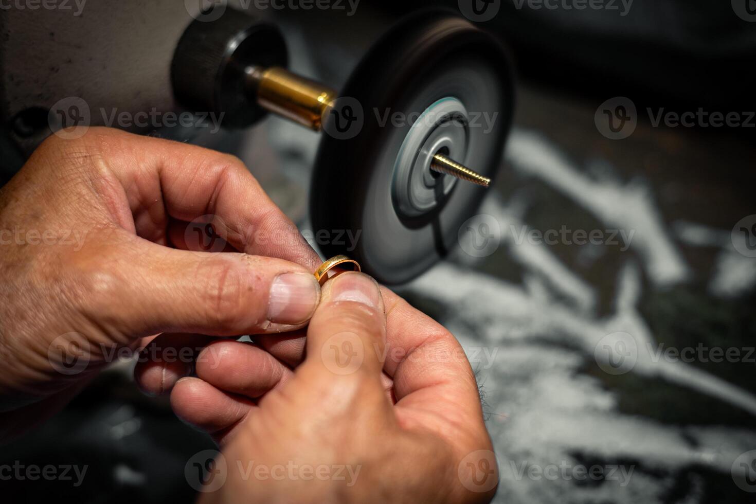 Goldsmith polishing a gold ring jewel in his jewelry workshop. Jeweler hands working in his craftwork studio. photo