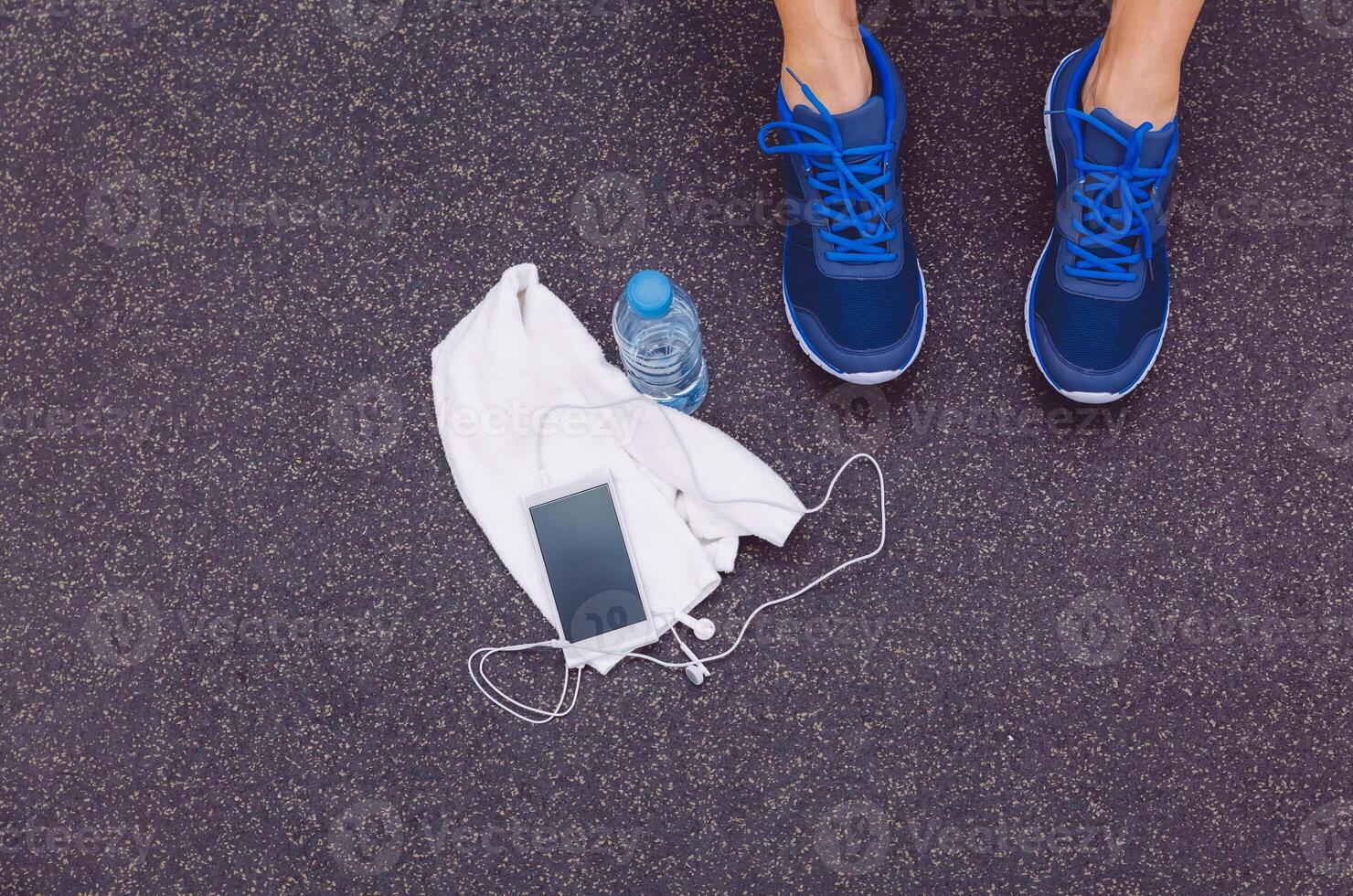 Man legs with sneakers, towel, water and smartphone in gym floor photo