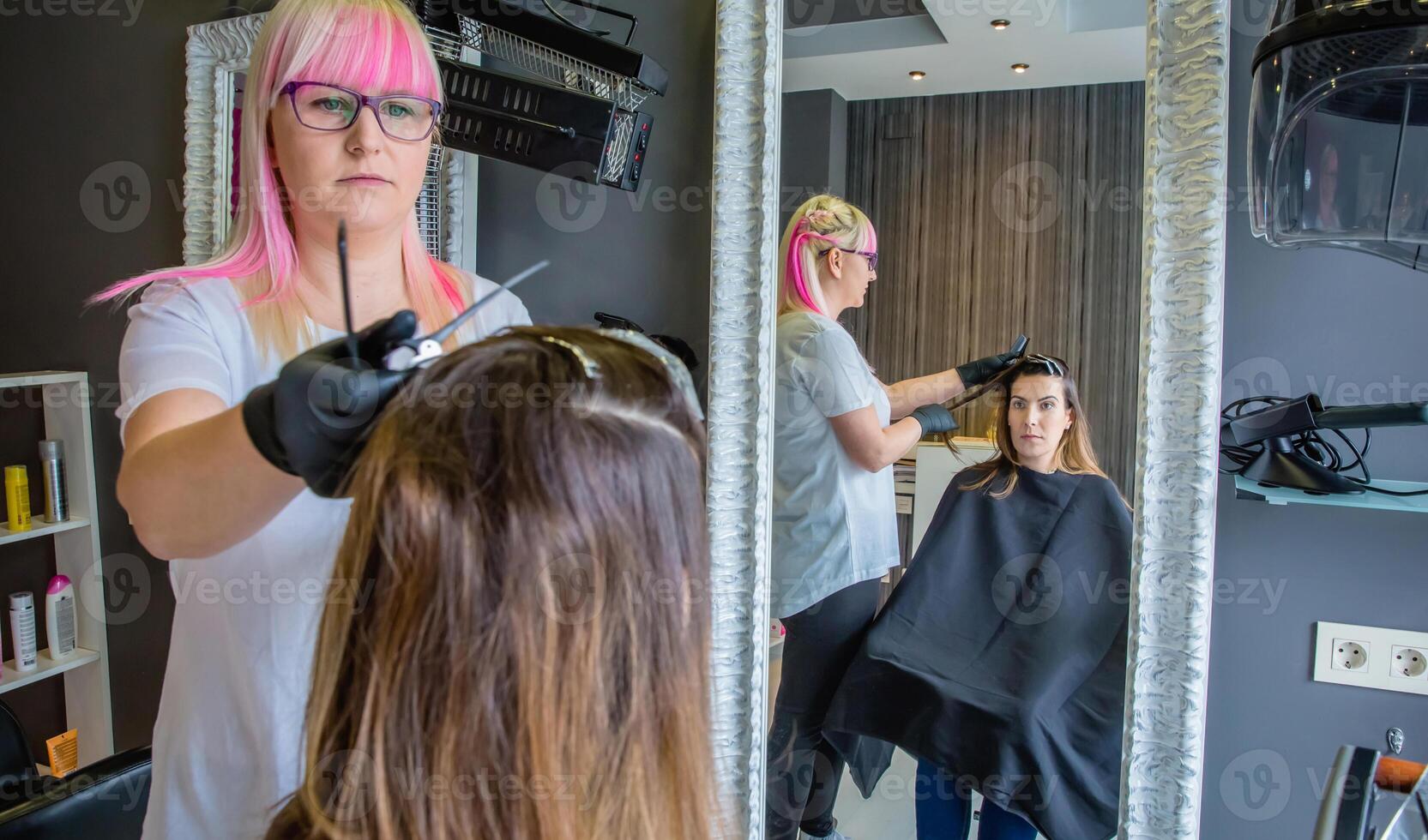 Woman looking in mirror to hairdresser combing hair photo