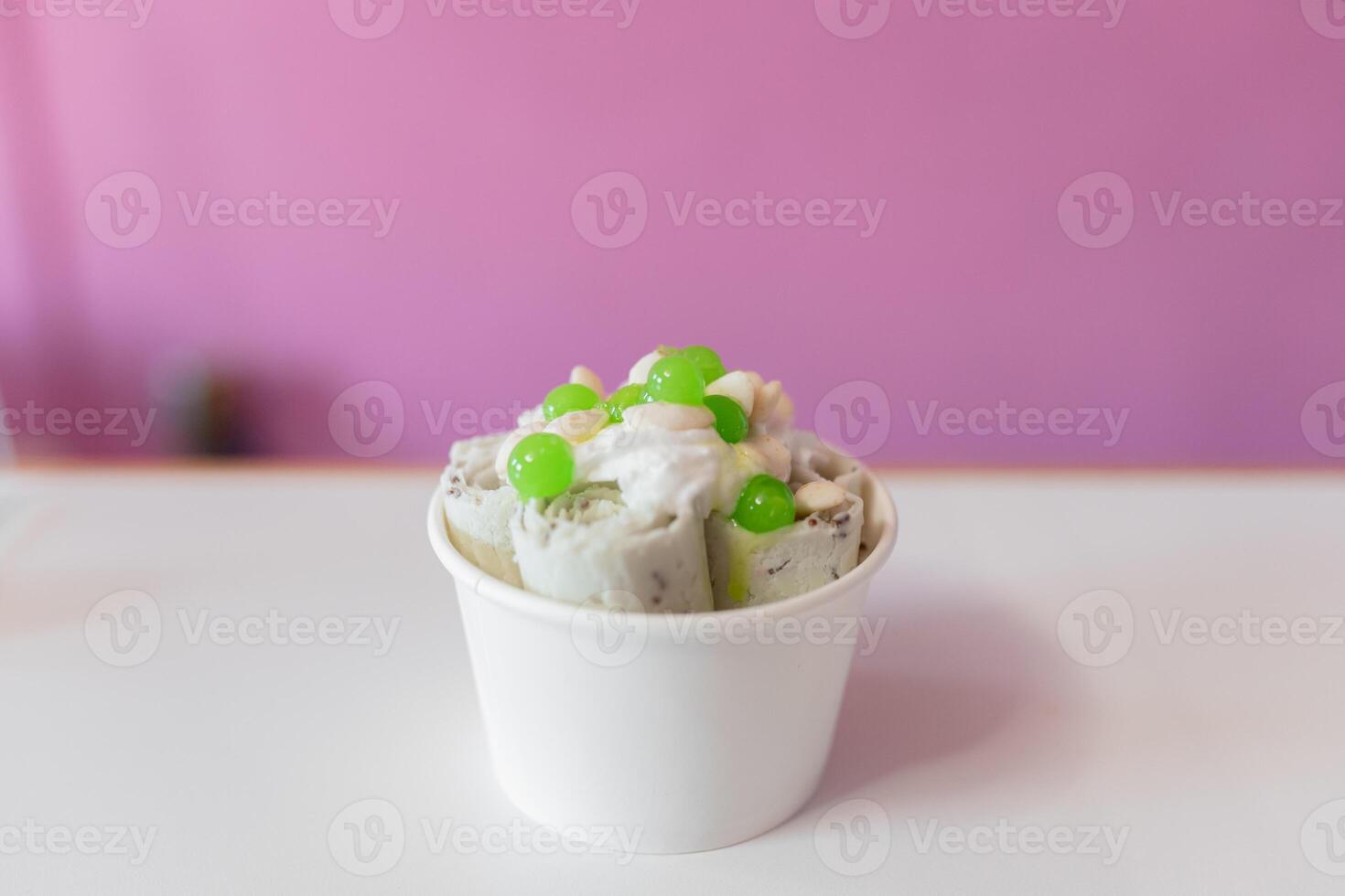 Close up of a rolled ice cream decorated with green bubbles and yogurt toppings photo