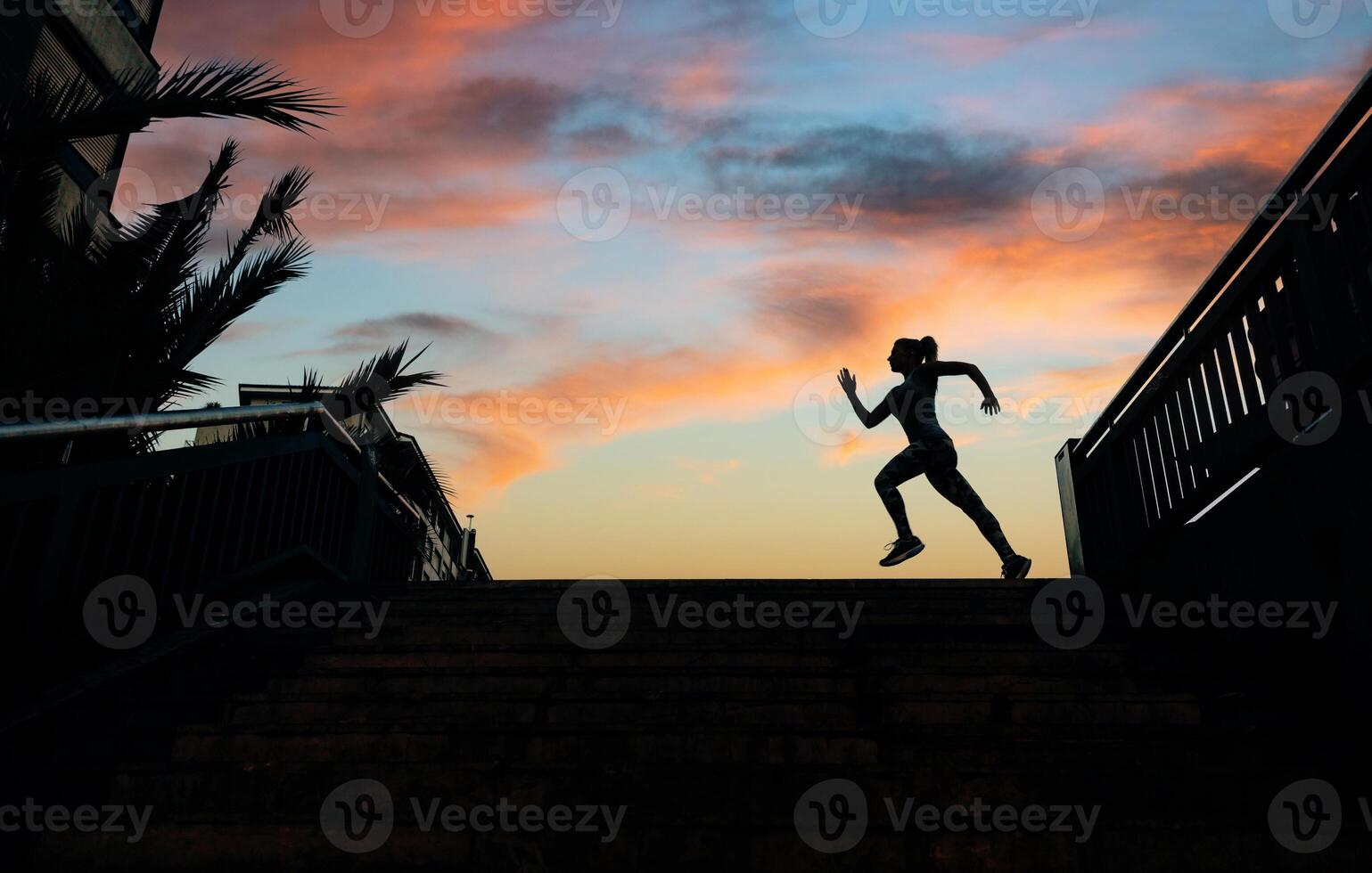 Female runner silhouette running over urban background with palm trees and sunset sky photo
