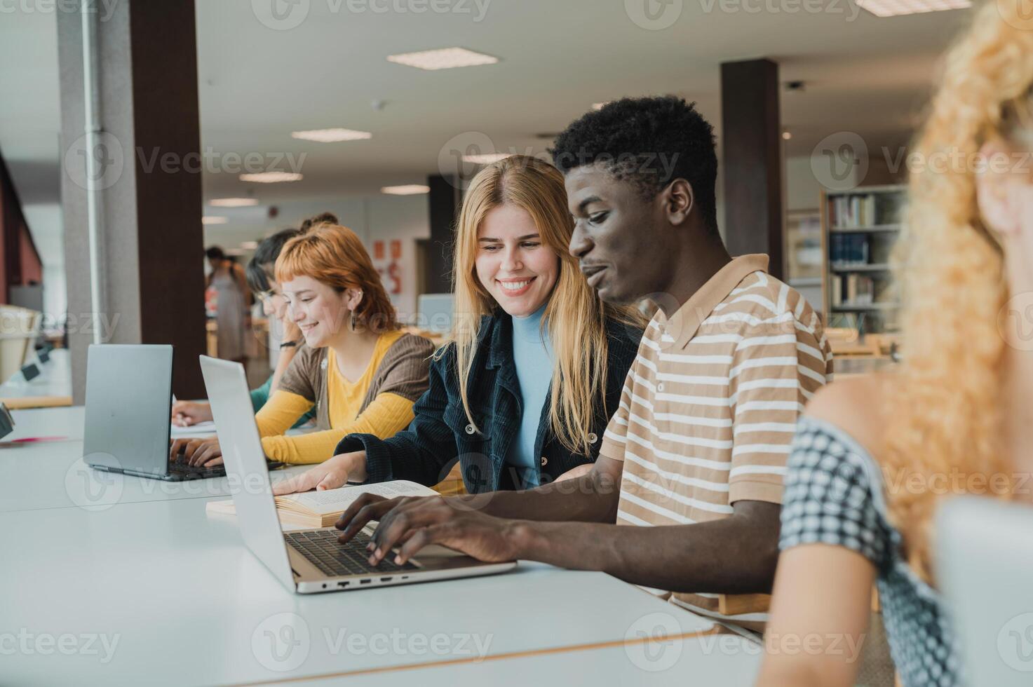 Cheerful diverse friends doing assignment using laptops in university photo