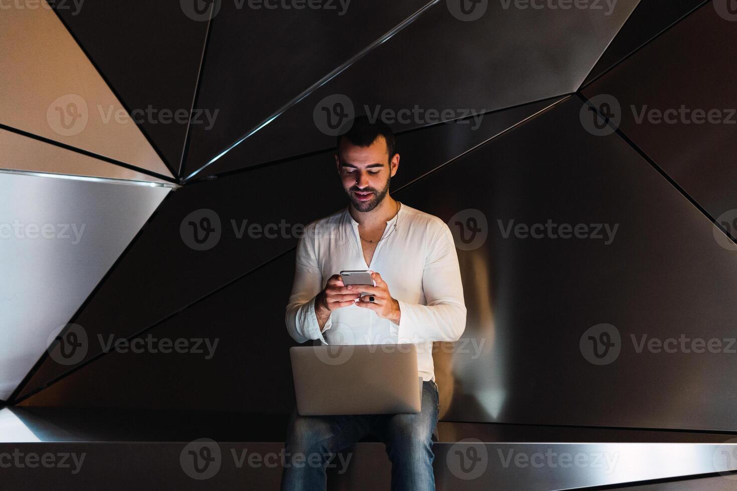 Man with laptop browsing smartphone in studio photo