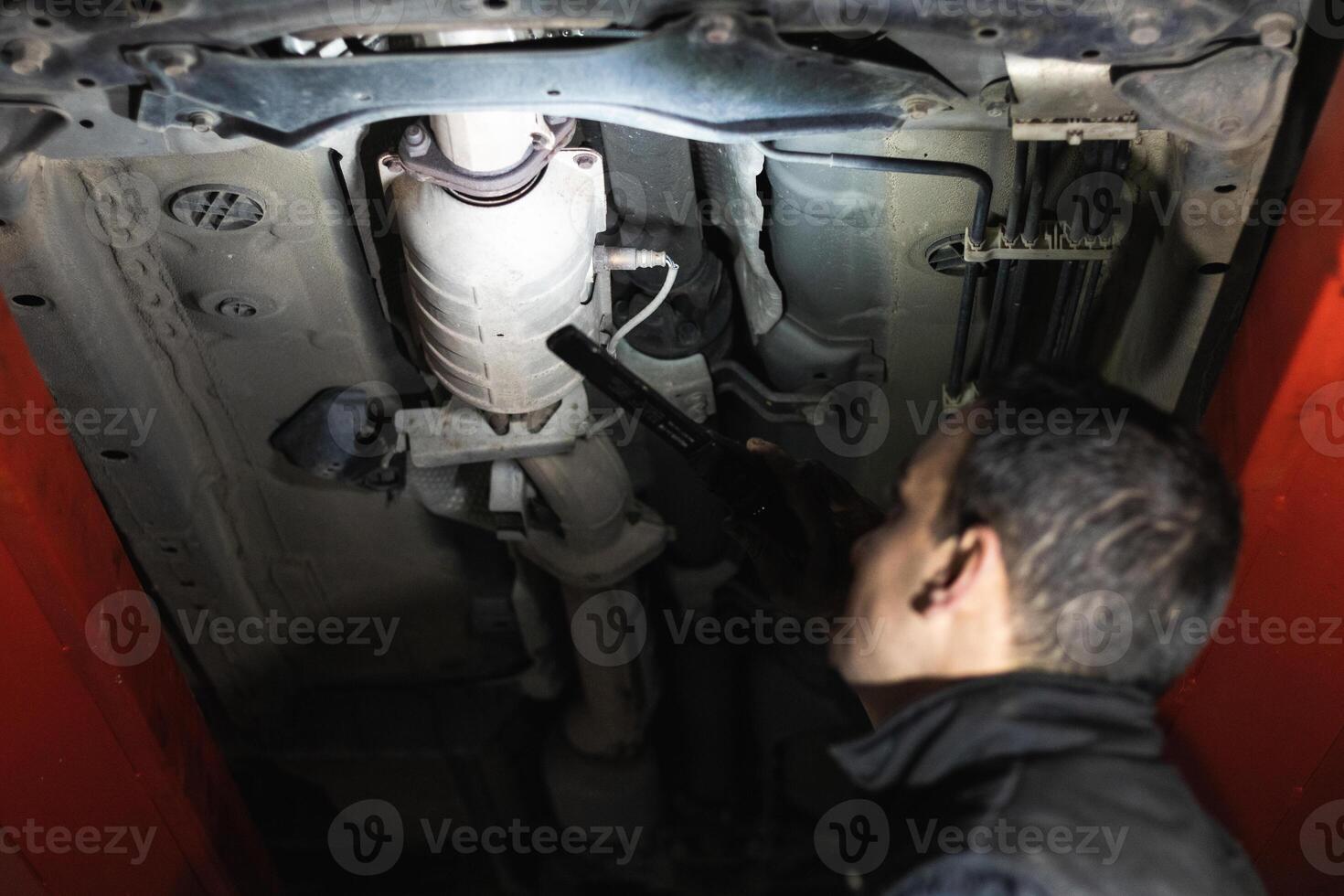 Anonymous repairman examining car exhaust system in garage photo