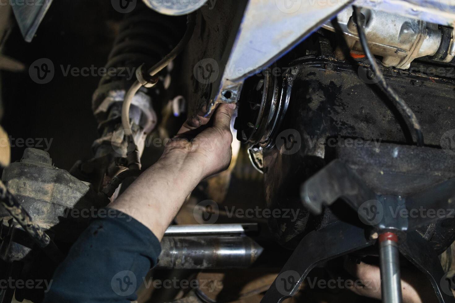 Anonymous adult repairman fixing car detail raised on lift in garage photo