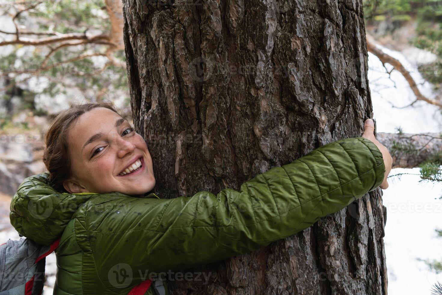 Smiling traveling woman hugging tree in woods photo