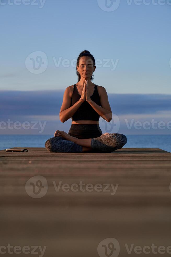 Peaceful Hispanic woman meditating on boardwalk near sea photo