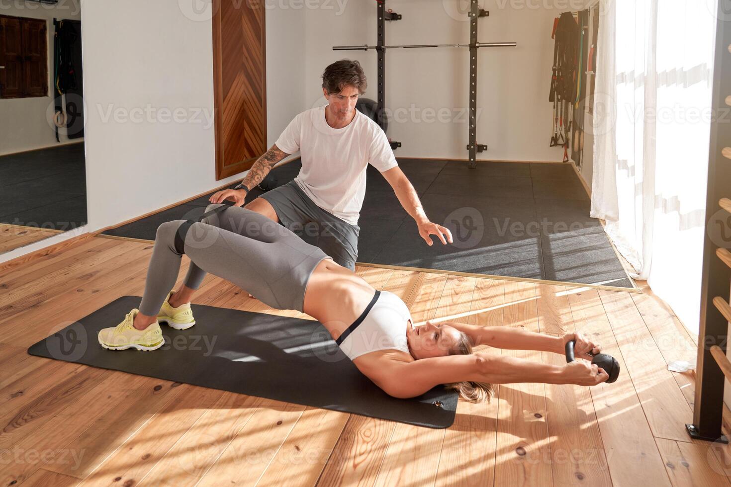 Male coach helping woman doing hip thrusts in gym photo