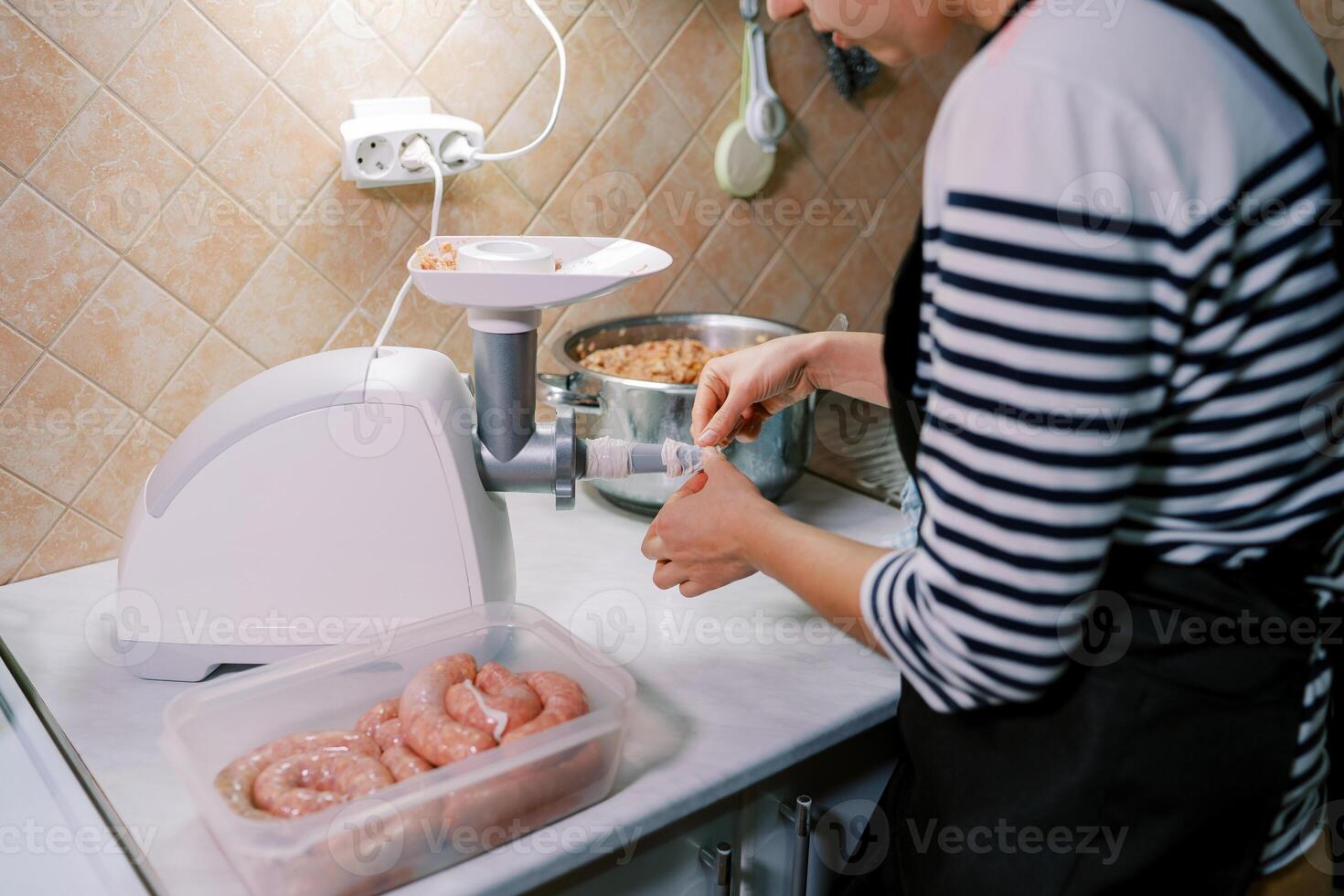 Woman stuffs intestines with minced meat in an electric meat grinder. Cropped photo