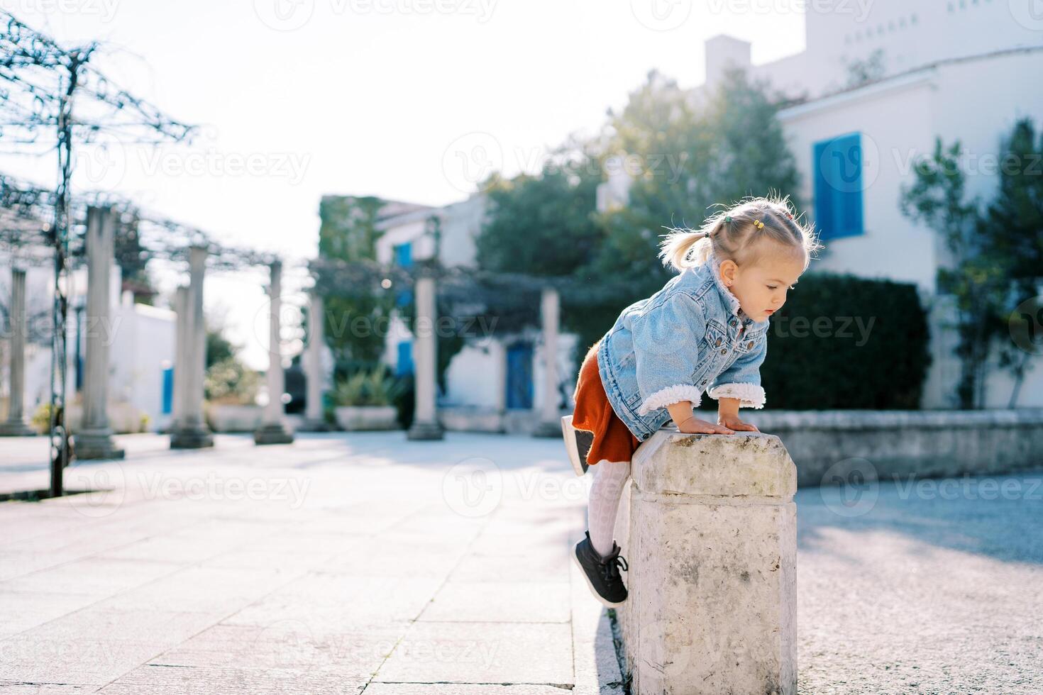 Little girl climbs a stone fence in the courtyard of the house photo